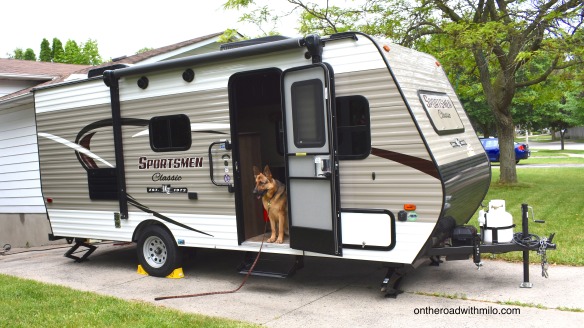 beige and white camper trailer with a black and tan german shepherd dog sitting in the doorway.