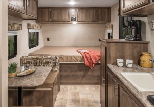 the bed, dinette, and kitchen of a camper,all in shades of brown